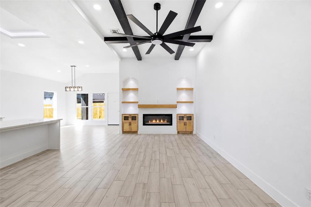 Living area featuring wood-finish tile flooring, recessed lighting, ceiling with dark decorative beams and a large ceiling fan, and a fireplace with built-in cabinetry and arched shelving