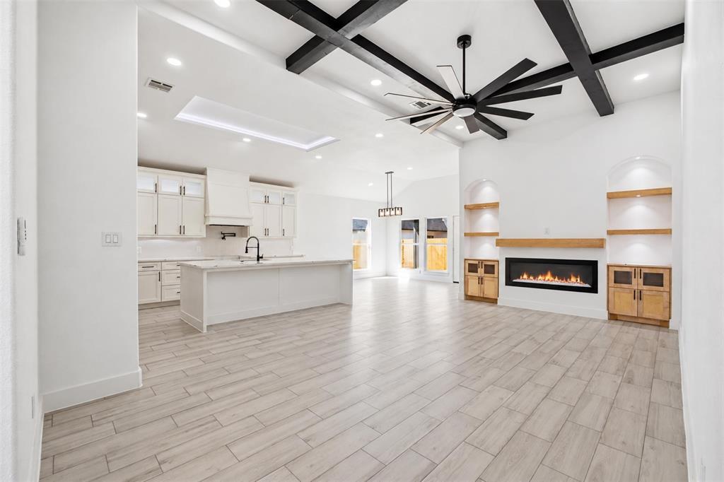 Open-concept space featuring vaulted ceilings with exposed wood-finish beams, wood-finish flooring, a linear fireplace with built-in shelving, a kitchen with a center island, and recessed lighting