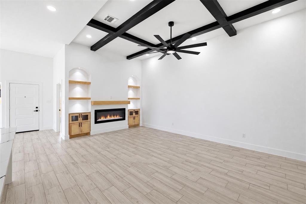 Living area featuring high ceilings with a dark-finished coffered beam design, wood-finish flooring, a contemporary electric fireplace with a wood mantel, and built-in recessed shelving