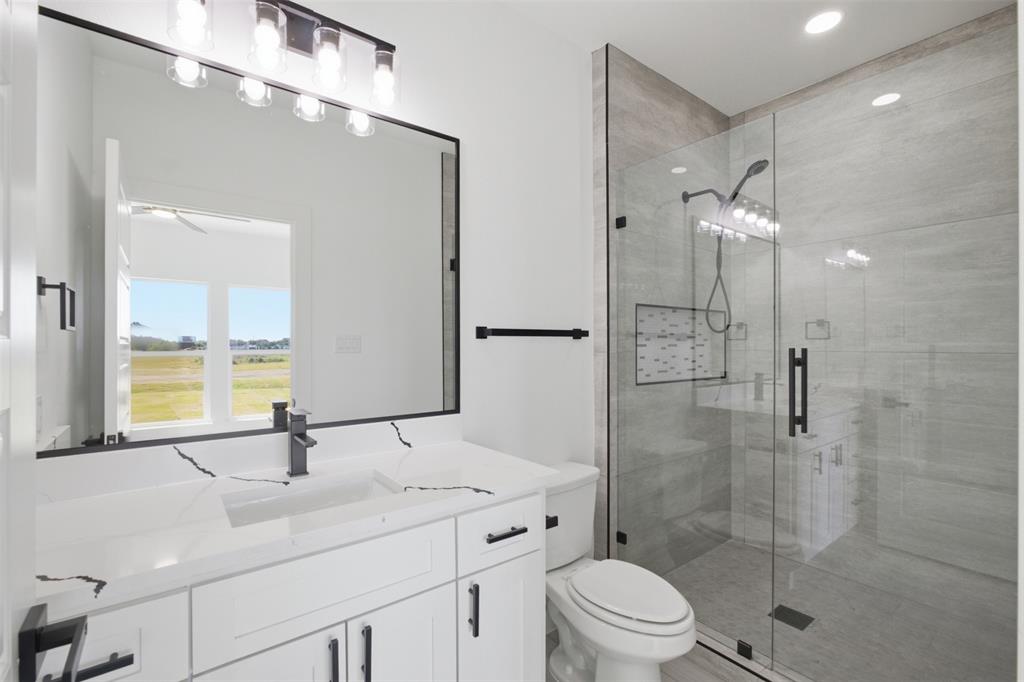 Bathroom featuring a white vanity with veined stone-finish countertop, undermount sink, frameless glass-enclosed shower with tile surround, and matte black fixtures
