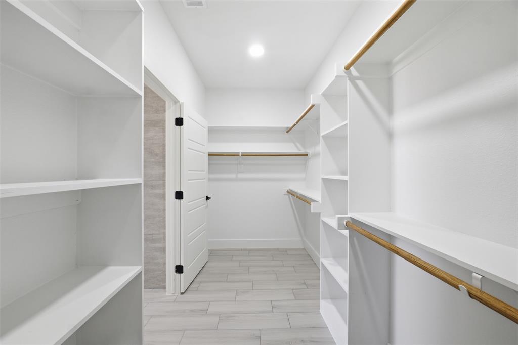 Walk-in closet featuring white built-in shelving, wooden garment rods, tile flooring, and a multi-panel door with black hardware