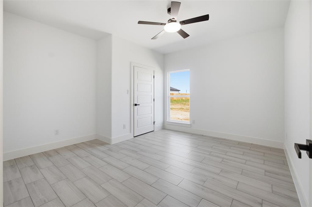Interior space featuring wood-finish flooring, a neutral color palette, a five-panel interior door with matte black hardware, and an integrated ceiling fan with light fixture