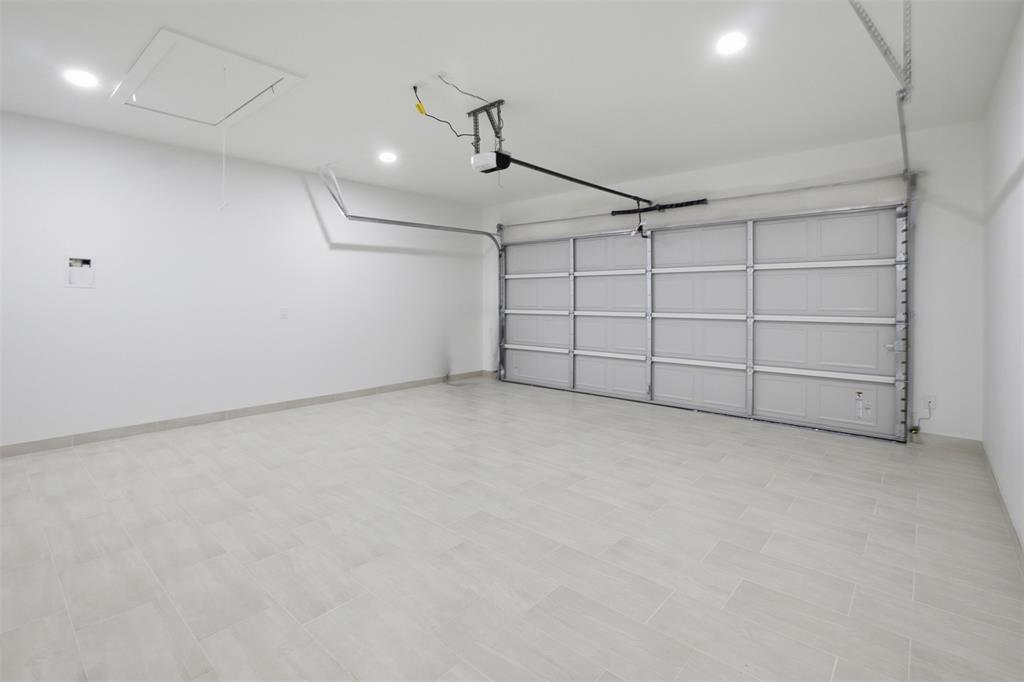 Multi-car garage featuring light-toned tile flooring, white walls, recessed ceiling lighting, and an overhead sectional door