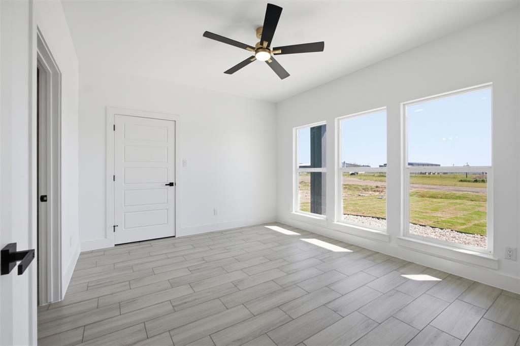 Neutral color palette featuring wood-finish flooring, three large windows, a four-panel interior door with matte black hardware, and a ceiling fan with integrated lighting