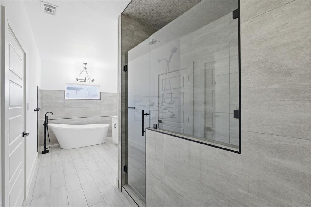 Freestanding soaking tub with matte black floor-mounted faucet, walk-in glass-enclosed shower with matte black hardware, and large-format tile wall and floor finishes
