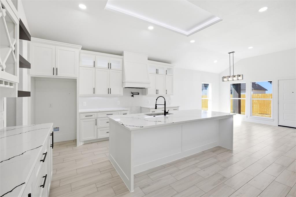 Kitchen featuring white shaker cabinetry, an expansive center island with veined stone-style countertops, recessed ceiling lighting, a matte black pot filler, and wood-finish flooring