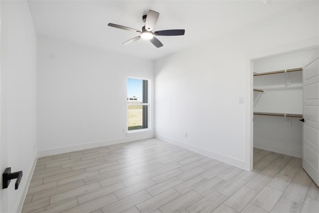 Wood-finish tile flooring, ceiling-mounted light fixture with fan, single-pane window, and walk-in closet with built-in shelving
