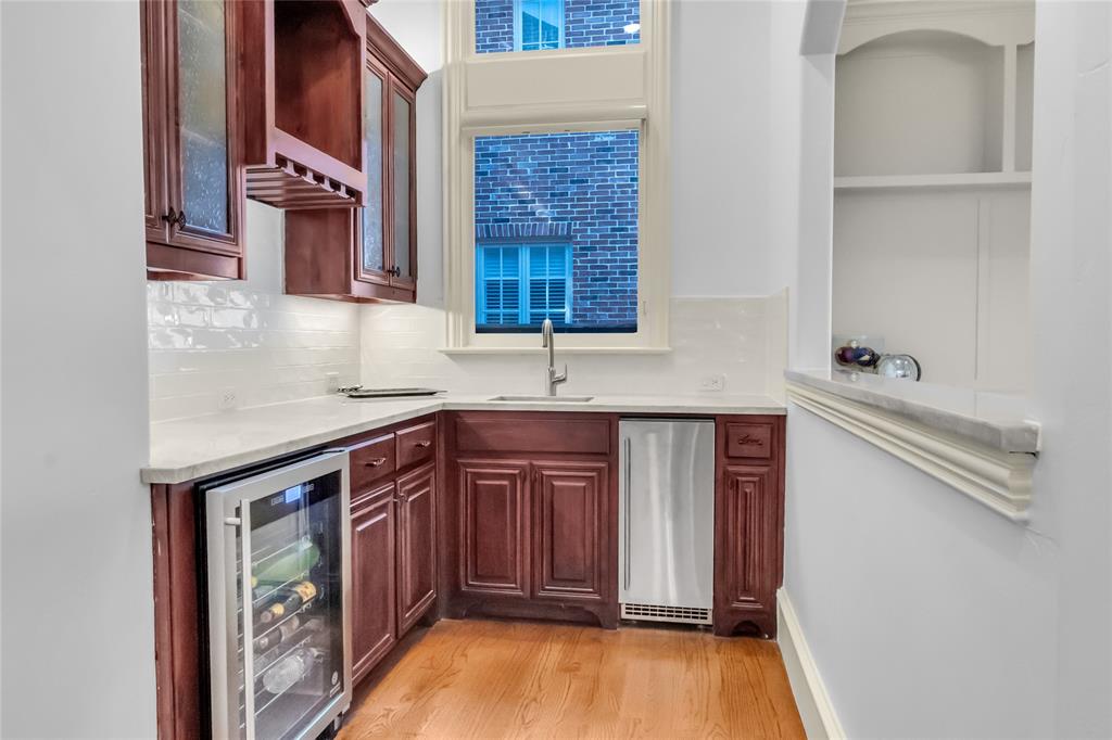 Custom cabinetry featuring a built-in wine rack, stone countertops, stainless steel under-counter beverage refrigerators, undermount sink, and recessed shelving