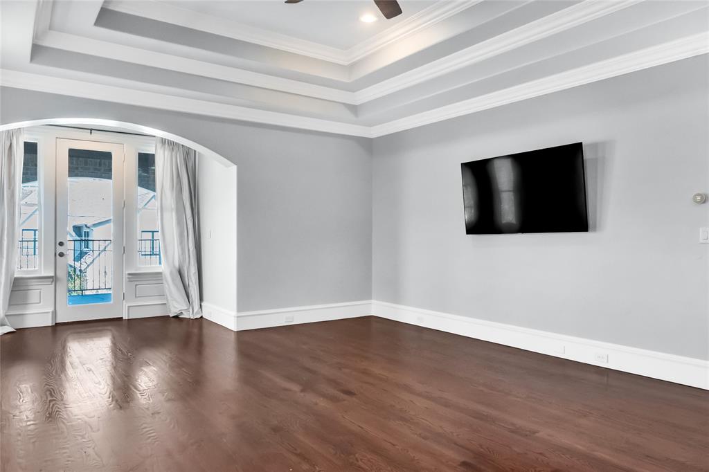 Tray ceiling, wood-finish flooring, arched doorway, and glass-paneled door