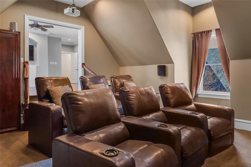 Vaulted ceiling with angled walls, carpeted flooring, wall-mounted speakers, ceiling-mounted projector, and window with casing