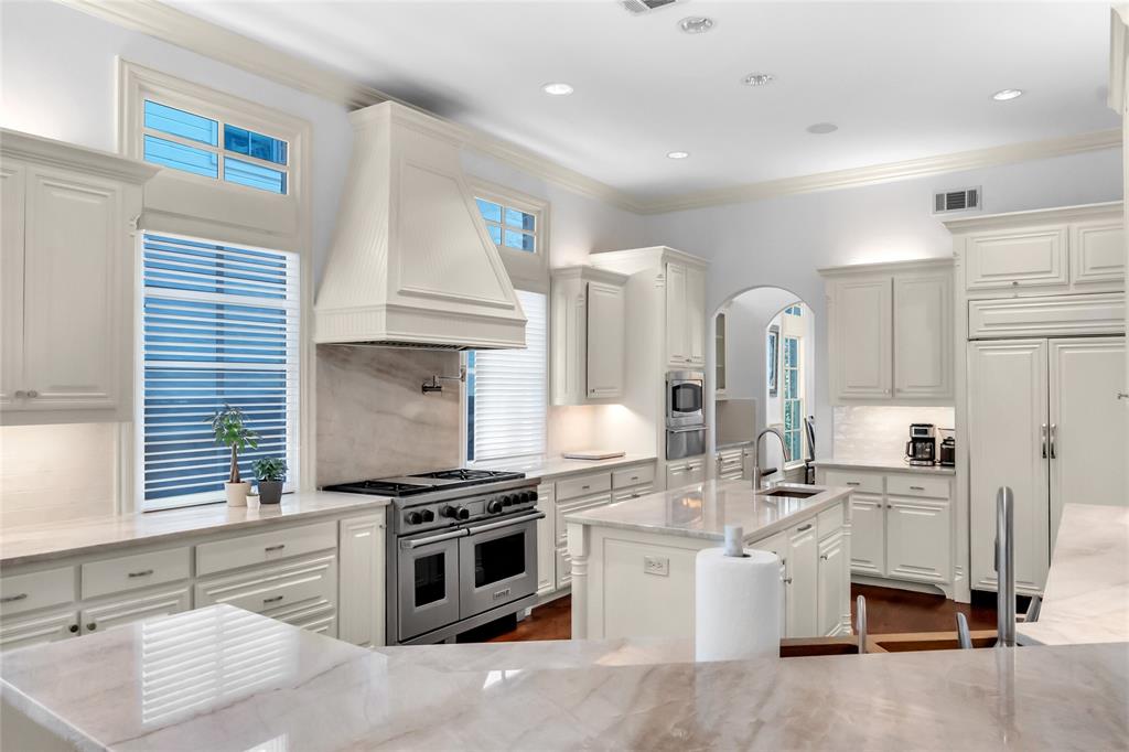 Kitchen featuring custom cabinetry, a stone-surround range hood, a stainless steel gas range, stone countertops, and a center island with an integrated sink
