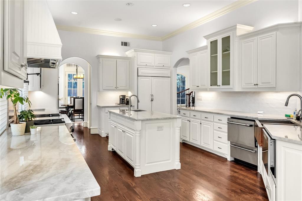 Kitchen featuring white cabinetry, stone countertops, a center island with an integrated sink, stainless steel appliances, and wood-finish flooring