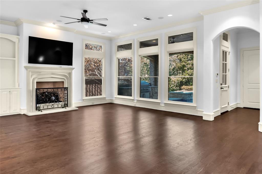 Living area featuring wood-finish flooring, tall windows, a built-in stone-surround fireplace, arched architectural detailing, and custom built-in cabinetry