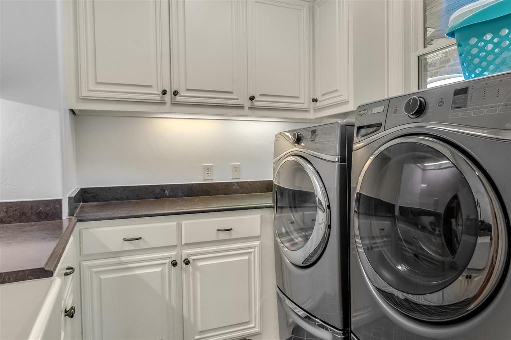 Laundry room featuring white shaker-style cabinetry, dark solid-surface countertops, and under-cabinet task lighting