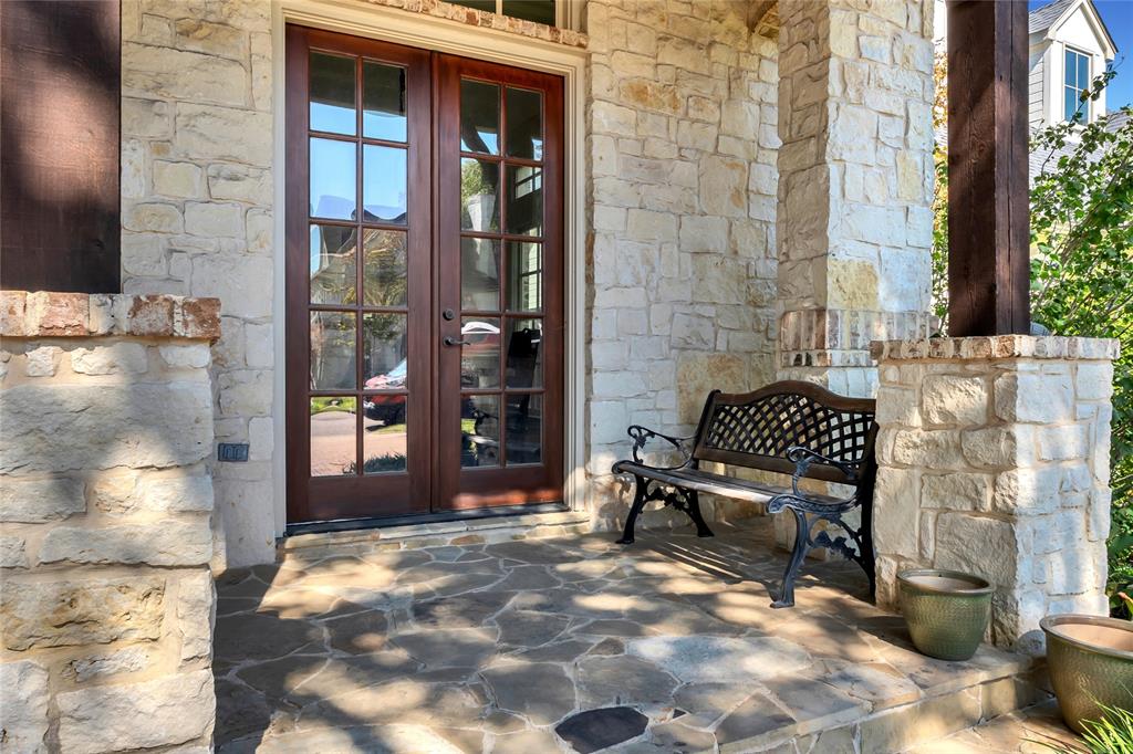 Covered porch featuring flagstone flooring, natural stone veneer columns, and glass-paneled double entry doors Covered porch featuring flagstone flooring, natural stone veneer columns, and glass-paneled double entry doors
