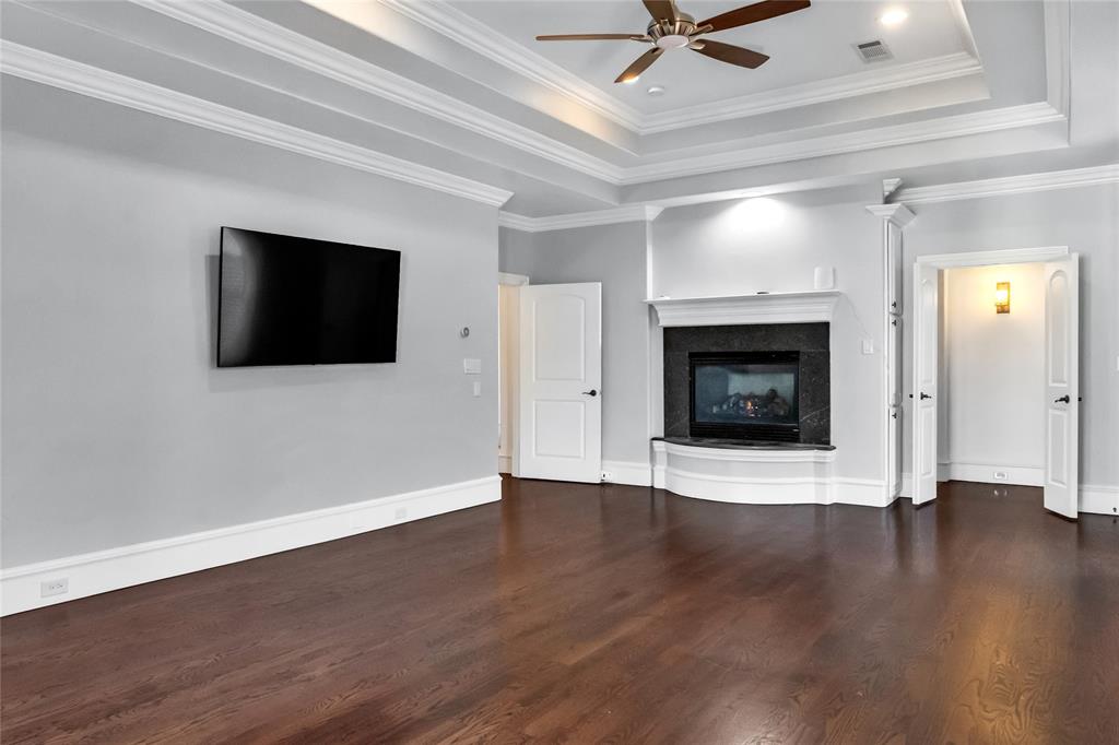 Tray ceiling with crown molding, wood-finish flooring, fireplace with stone surround and mantle, and ceiling fan