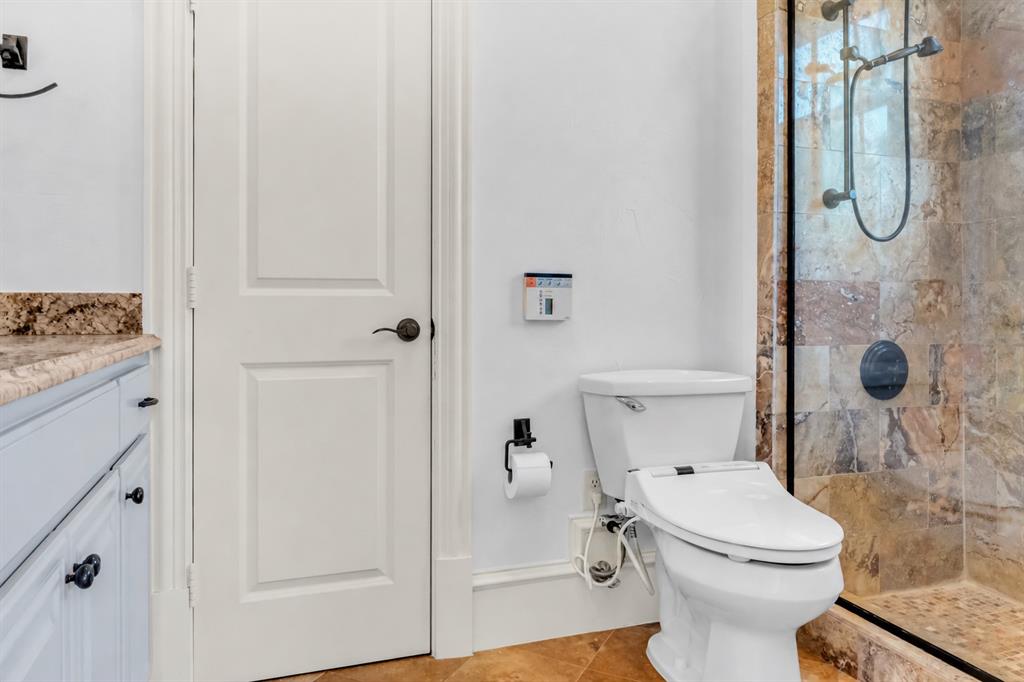 Bathroom featuring a walk-in shower with stone tile surround, natural stone flooring, vanity with stone countertop, and matte black hardware