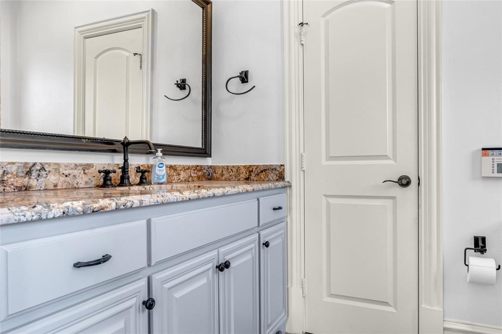 Vanity featuring a stone-surface countertop, dark-finish widespread faucet, and paneled cabinetry with matte black hardware, paired with a framed wall-mounted mirror