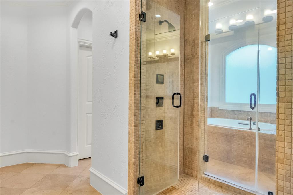 Walk-in shower featuring a frameless glass door, multi-function wall-mounted showerhead, and mosaic tile surround, paired with a deep soaking tub set beneath an arched window