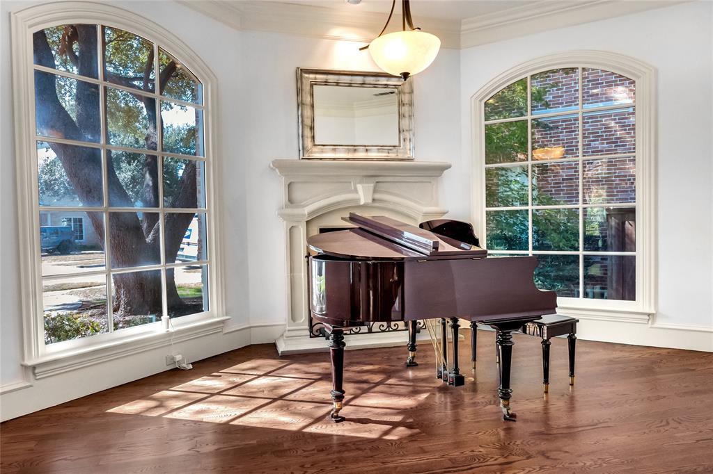 Wood-finish flooring, fireplace with a custom stone surround, two oversized arched windows with muntin detailing, and a pendant light fixture Wood-finish flooring, fireplace with a custom stone surround, two oversized arched windows with muntin detailing, and a pendant light fixture