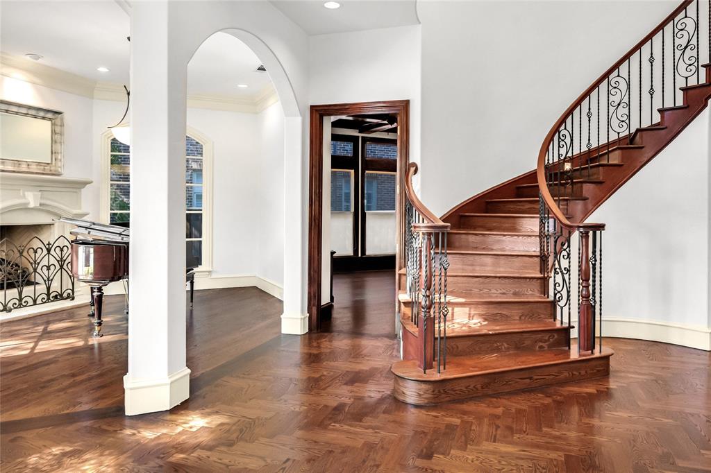 Foyer featuring herringbone wood-finish flooring, a curved staircase with ornate iron balusters, an arched architectural opening, and a decorative fireplace mantel Foyer featuring herringbone wood-finish flooring, a curved staircase with ornate iron balusters, an arched architectural opening, and a decorative fireplace mantel
