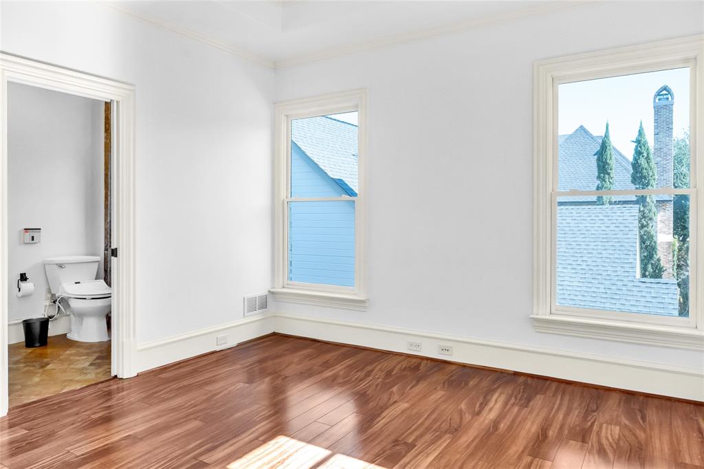 Wood-finish flooring, white walls, crown molding, and two windows with exterior casing