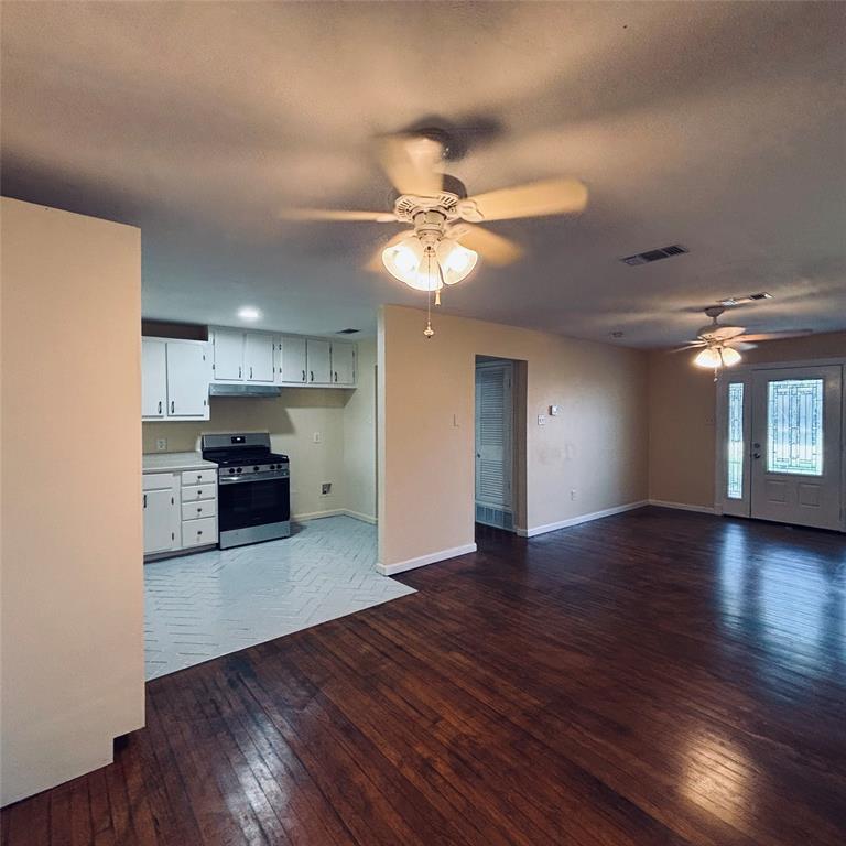 Wood-finish flooring, kitchen featuring white cabinetry and stainless steel range, herringbone-patterned flooring in kitchen, two ceiling fans with integrated lighting, and an entry door with decorative glass paneling