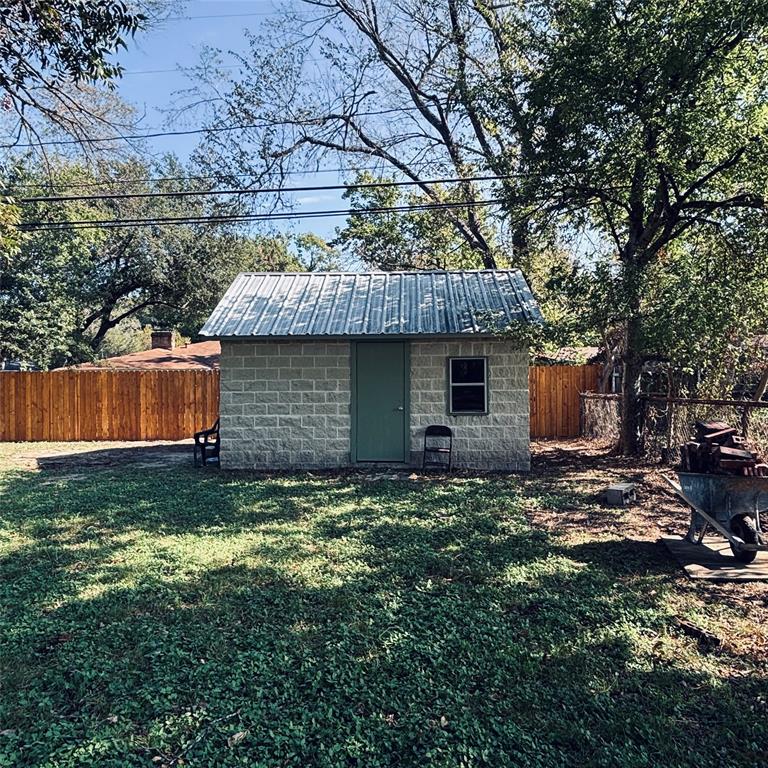 Detached outbuilding featuring a concrete block exterior, a metal gable roof, and wood-style perimeter fencing