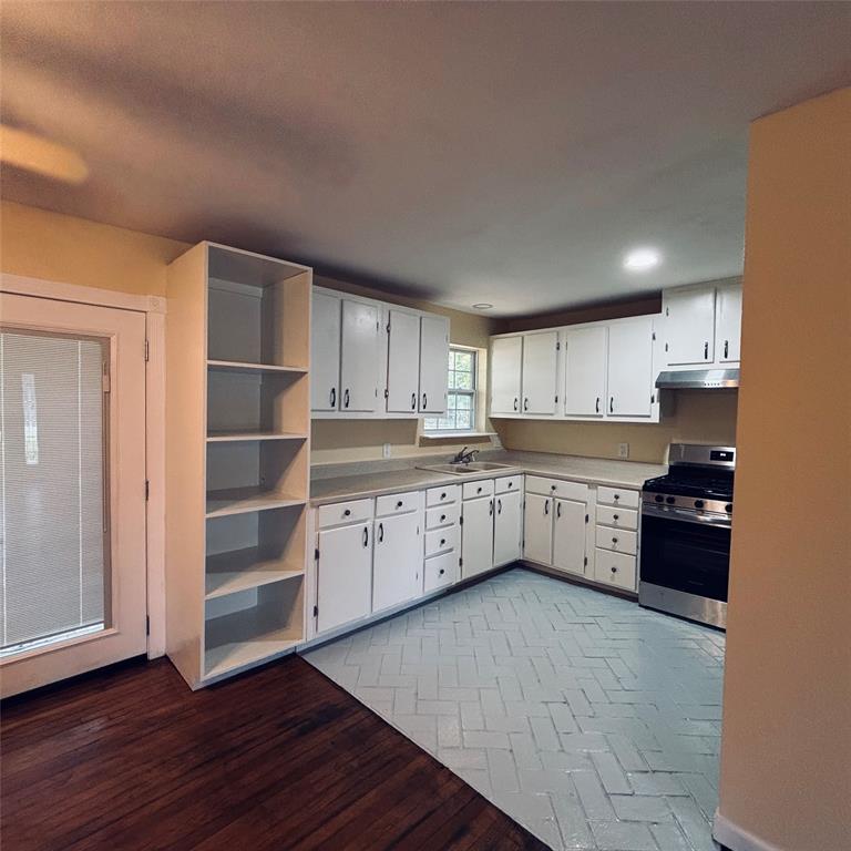 Kitchen featuring white cabinetry, built-in open shelving, stainless steel range with overhead vent, and painted herringbone-patterned flooring