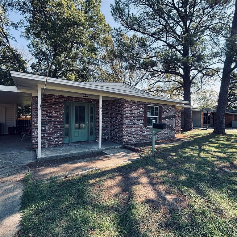 Single-story brick exterior featuring a covered front porch, attached carport, mature trees, and a front entry with glass-paneled sidelights