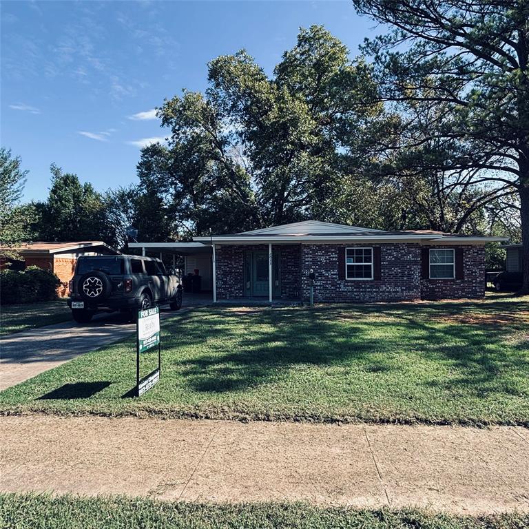 Single-story brick exterior featuring a covered carport, concrete driveway, and mature trees