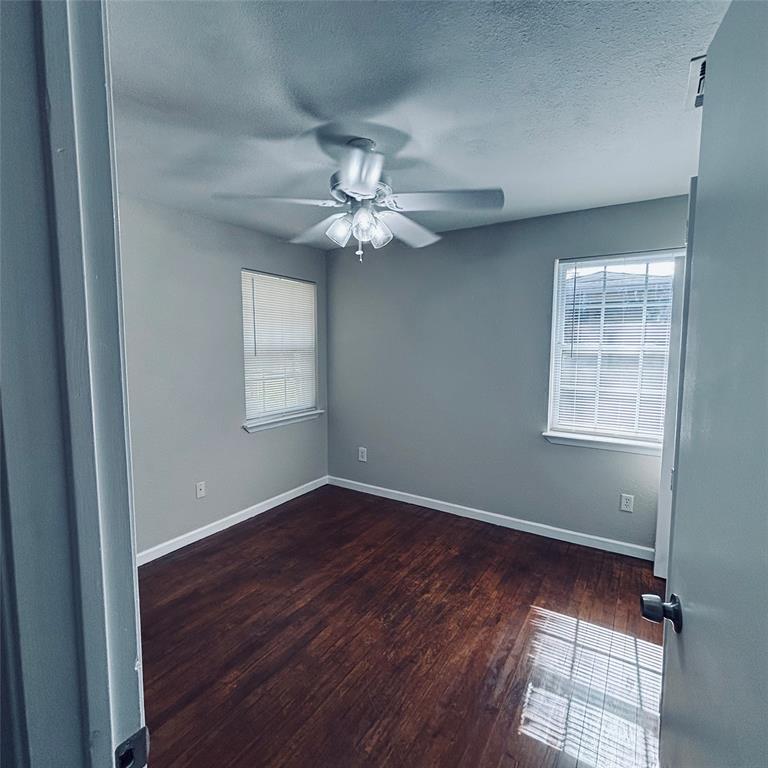Room featuring dark wood-finish flooring, two windows with horizontal blinds, and a central ceiling fan with integrated lighting