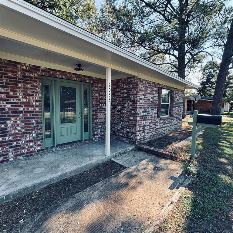 Brick exterior featuring a covered entryway, paneled front door with sidelights, concrete porch, and mature trees