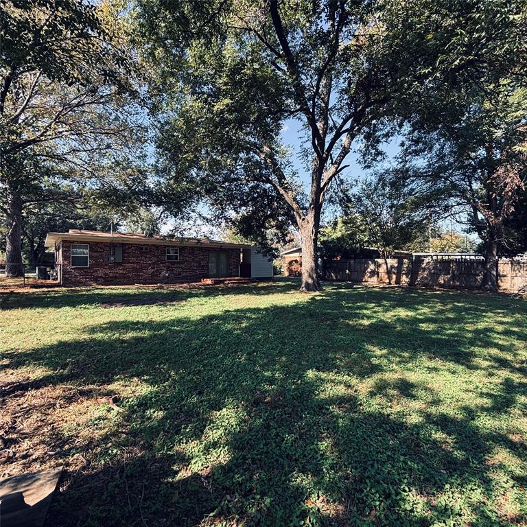 Expansive backyard featuring a brick exterior, mature trees, and a wooden privacy fence