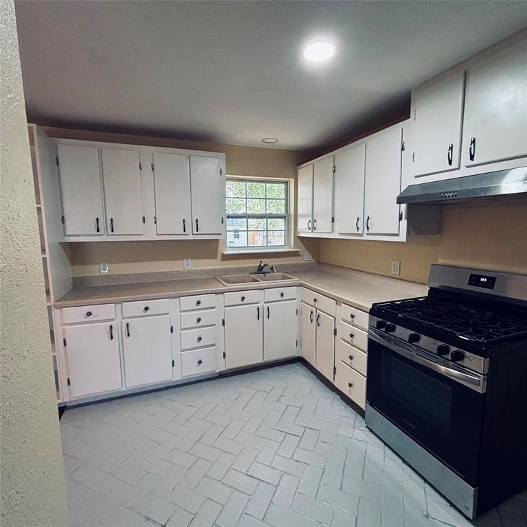 Kitchen featuring white cabinetry, solid-surface countertops, dual-basin sink, integrated stainless steel range hood, and herringbone-patterned tile flooring
