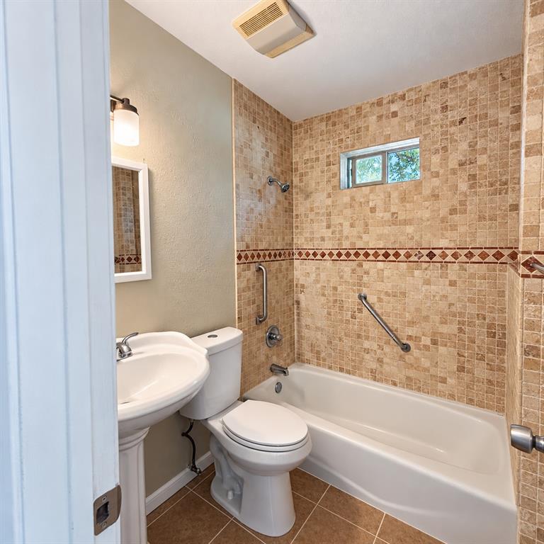 Bathroom featuring a pedestal sink, porcelain tub, mosaic tile surround with a decorative border, and wall-mounted metal grab bars