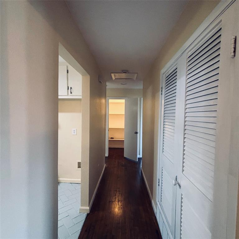 Hallway featuring dark wood-finish flooring, white louvered closet doors, and a tiled utility area with white upper cabinetry