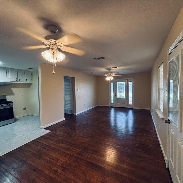 Interior featuring wood-finish flooring, dual ceiling fans with integrated lighting, white kitchen cabinetry, and an exterior door with glass panes