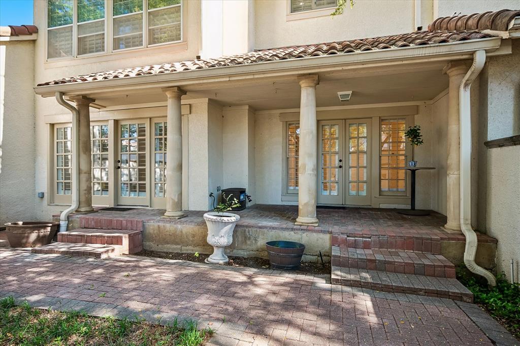 Covered patio featuring classical columns, terracotta tile roofing, multi-pane glass French doors, and patterned brick paving
