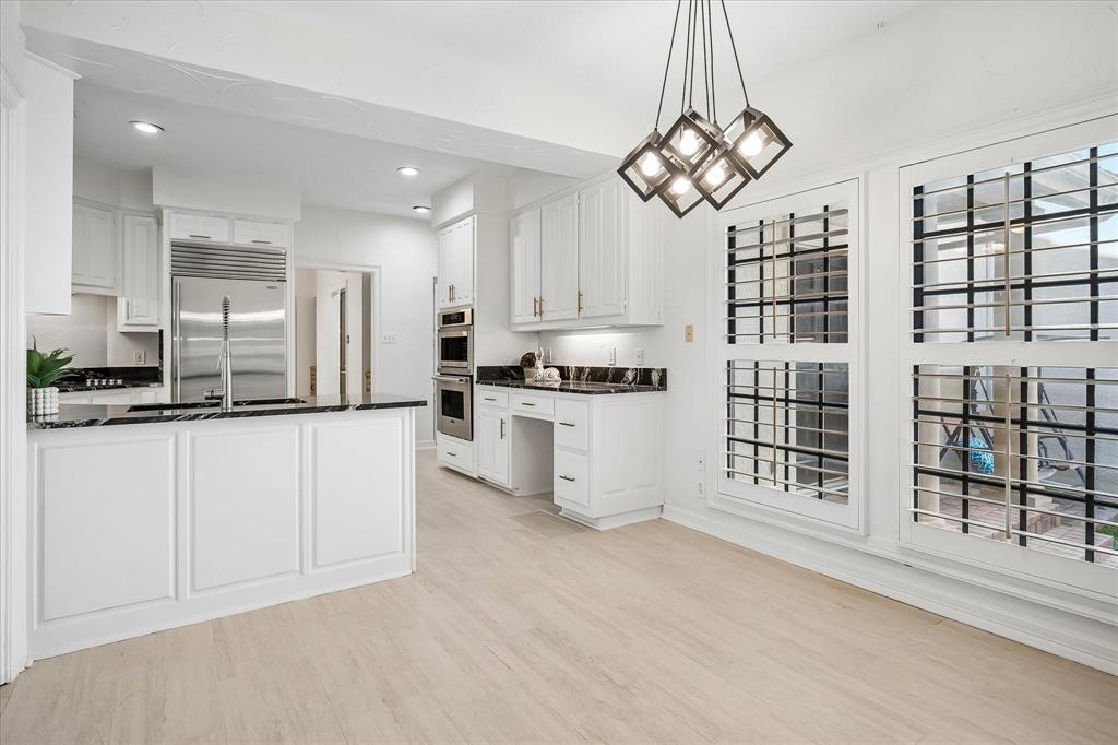 Kitchen featuring white cabinetry, dark stone countertops, stainless steel appliances including a built-in double oven and refrigerator, wood-finish flooring, and geometric pendant lighting