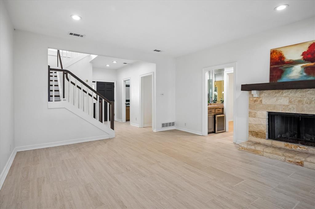 Open-concept living space featuring wood-finish flooring, recessed lighting, a floor-to-ceiling stone fireplace with a substantial timber mantel, and a staircase with white balusters and a dark wood handrail