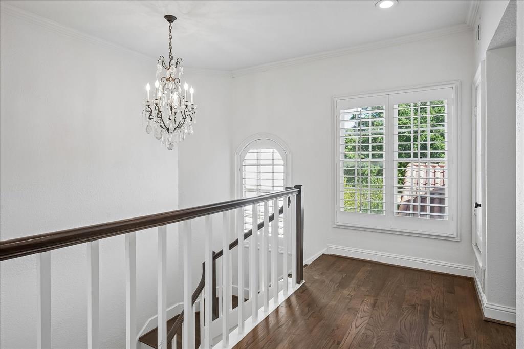Landing area featuring wood-finish flooring, a tiered crystal chandelier, white balustrades with a dark wood handrail, arched windows, and white plantation shutters