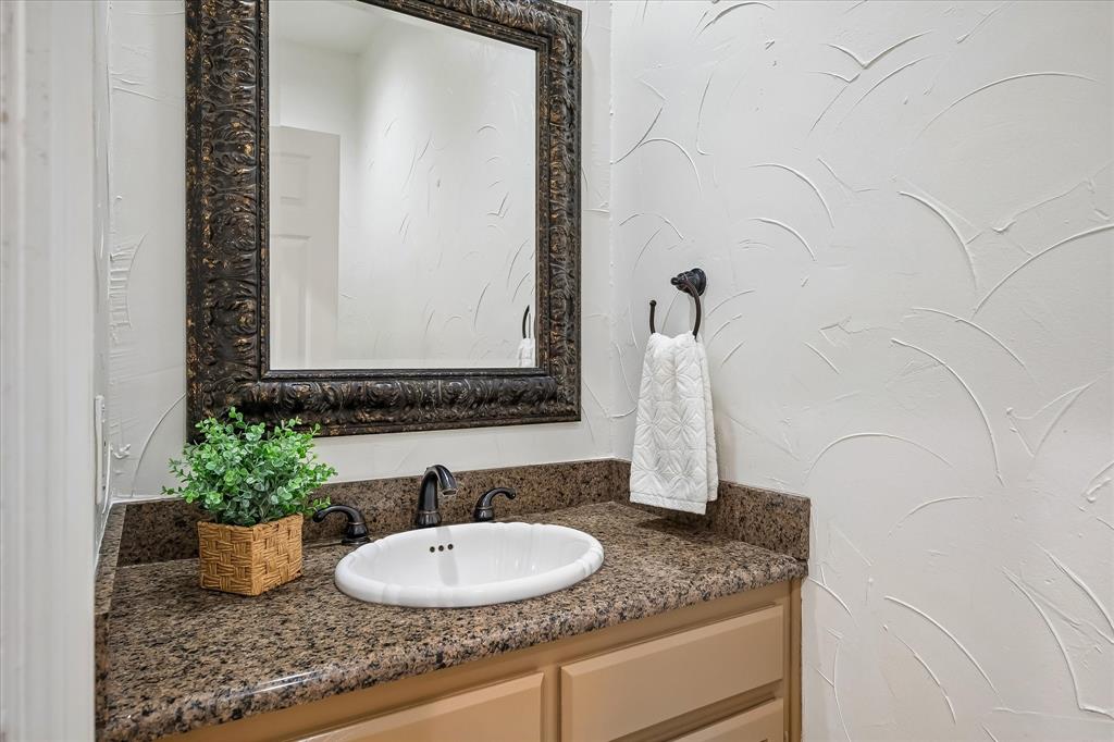 Vanity featuring stone-finish countertop, oval drop-in sink, dark metal widespread faucet, decorative framed mirror, and textured wall finish
