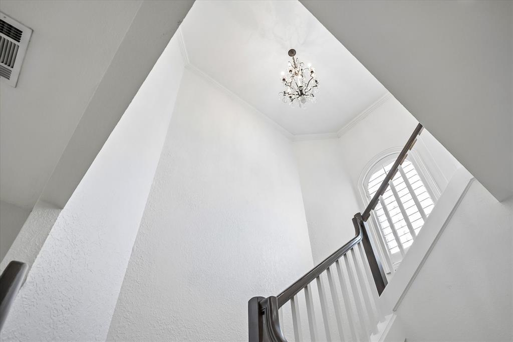 High-ceilinged entry featuring a tiered crystal chandelier, arched window with plantation shutters, and a staircase with white vertical balusters and a dark wood handrail