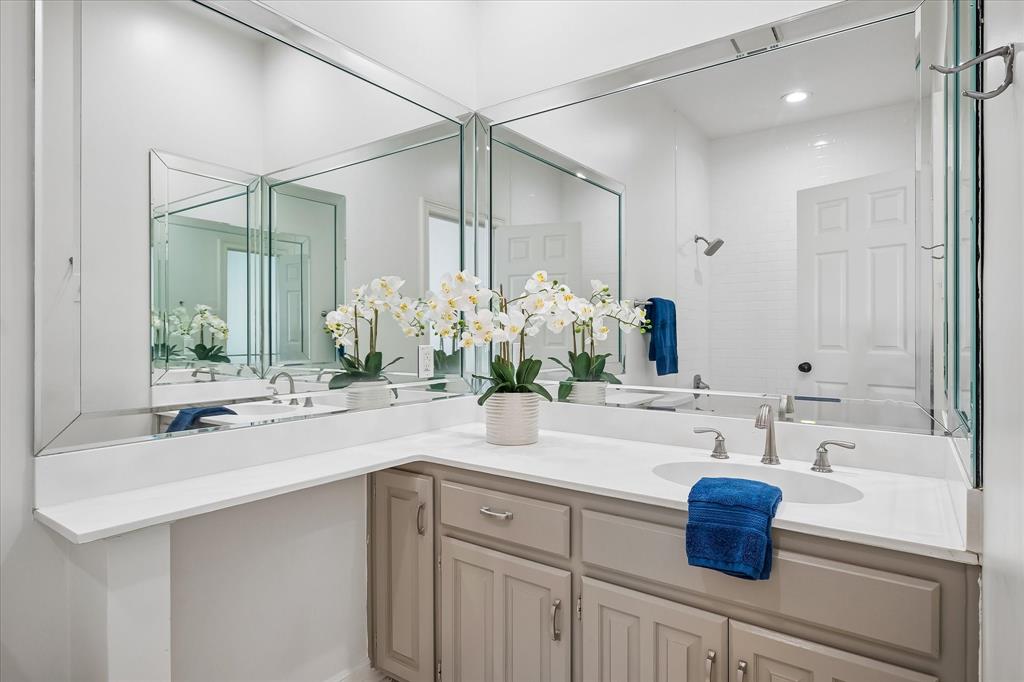 L-shaped vanity featuring light-toned cabinetry, solid surface countertop, undermount sink, widespread faucet, and expansive wall-to-wall beveled mirrors