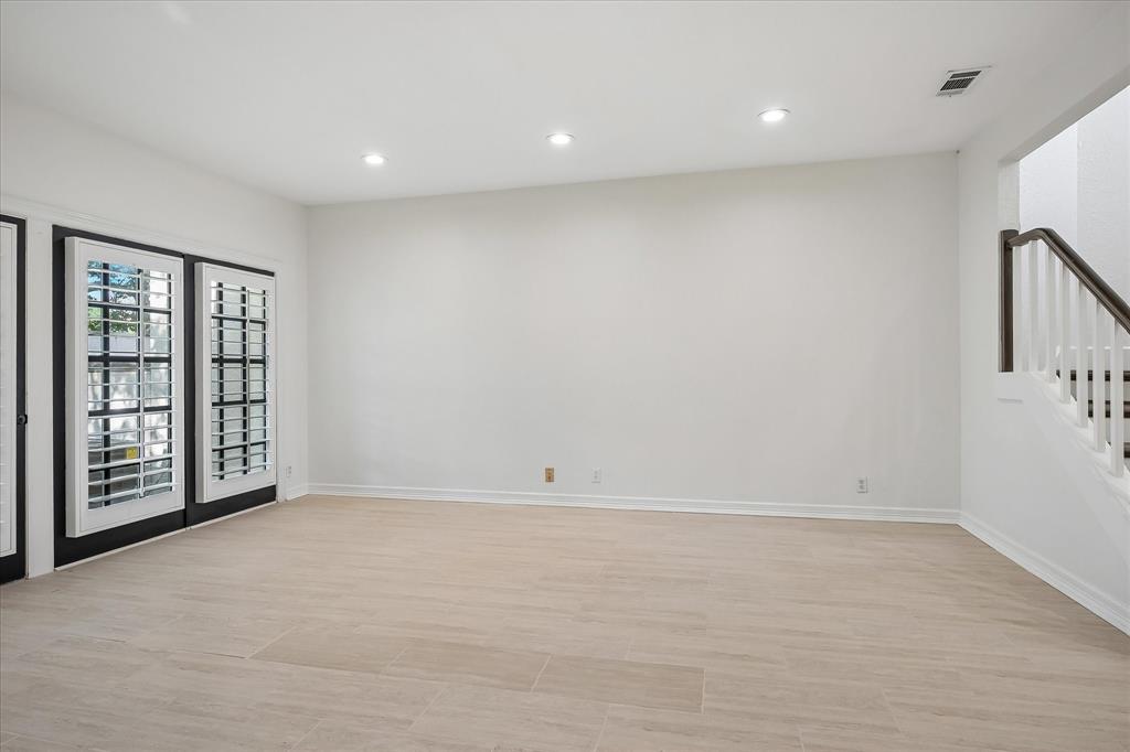 Neutral-toned wood-finish flooring, recessed lighting, and double glass-paneled doors with interior plantation shutters