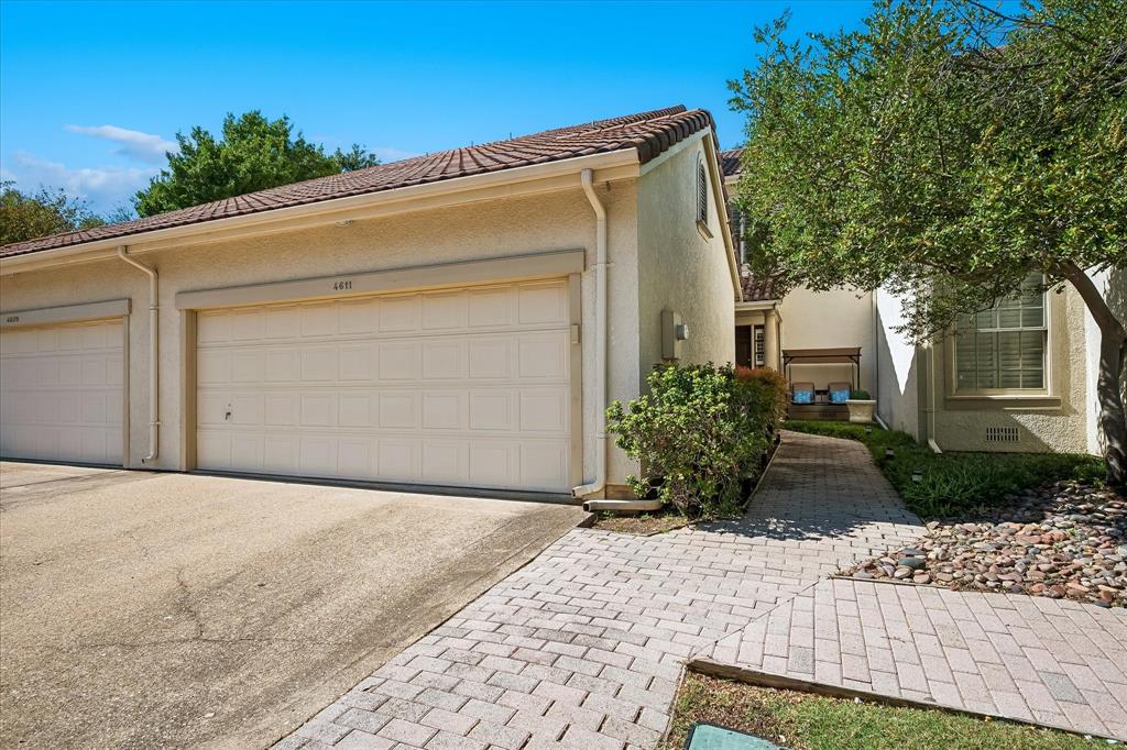 Stucco exterior featuring a two-car garage with paneled doors, a tiled roof, and a paver walkway