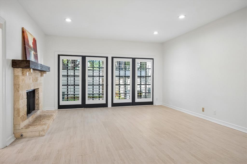 Fireplace with natural stone surround and timber mantel, wood-finish flooring, recessed lighting, and double-paned French doors with grid detailing