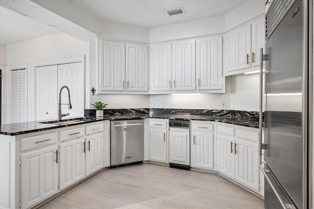 Kitchen featuring white shaker-style cabinetry, dark stone countertops with contrasting veining, stainless steel appliances, a high-arc pull-down faucet, and light-toned tile flooring