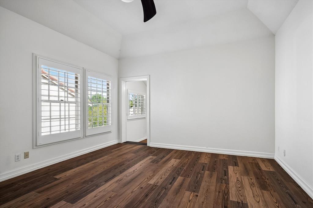 Vaulted ceiling featuring a central ceiling fan, VLP flooring, and windows with plantation shutters